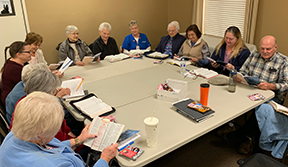 eleven adults sitting around large table during bible study
